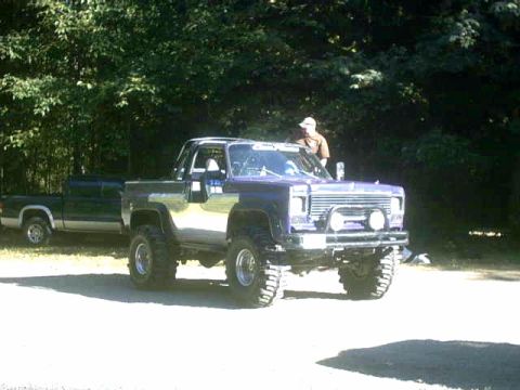 1976 Chevrolet C/K Pickup - Lifted pickup truck with chrome trim and off-road tires parked next to a dark green pickup truck.