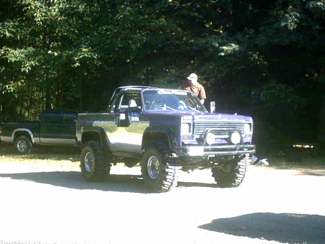 Lifted pickup truck with chrome trim and off-road tires parked next to a dark green pickup truck