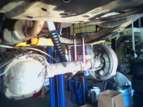 1993 Ford Bronco - The underside of a vehicle is shown, focusing on the rear axle, leaf springs, and shock absorber, with a lift in the background.