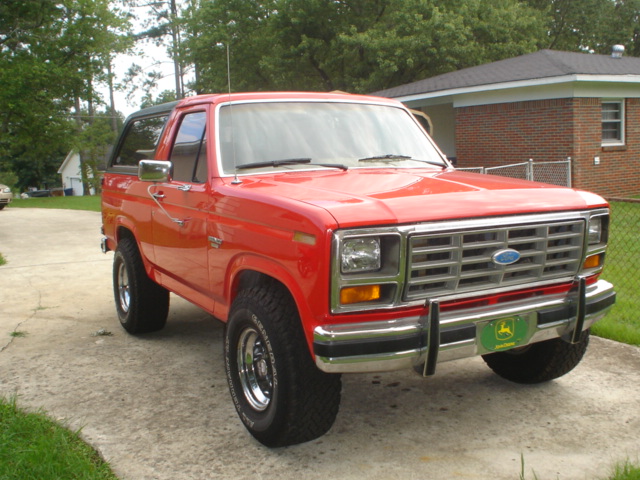 Red 1985 Ford Bronco front 3/4 view with chrome grille and John Deere plate