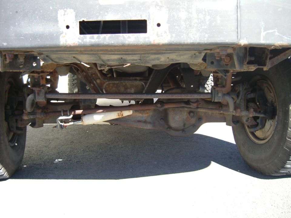 Underside front view of a truck's solid front axle, steering linkage, and white stabilizer shock