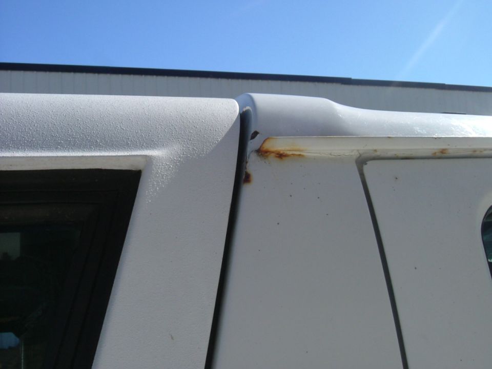 Rust bleeding along the drip-rail seam of a white SUV hardtop rear corner