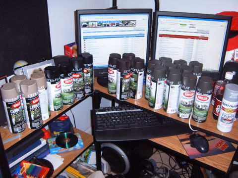 1988 Ford Bronco - A collection of spray paint cans is organized on a desk next to computer monitors and a keyboard.