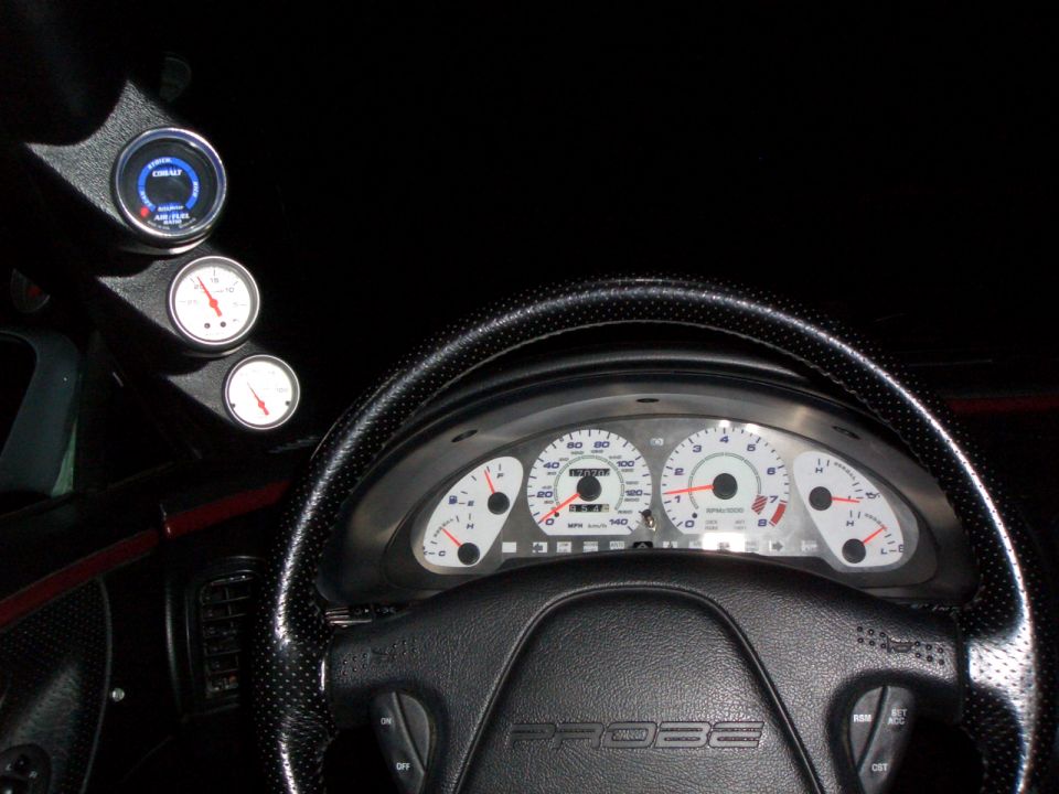 Probe gauge cluster lit white with leather steering wheel and three pillar-mounted gauges