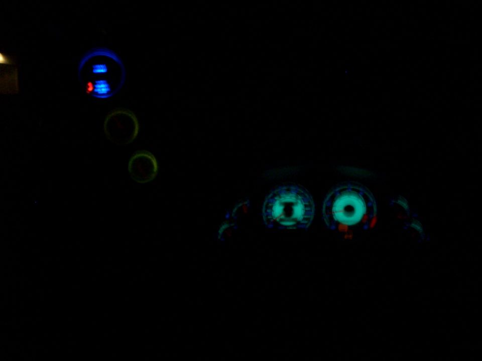 Glowing teal speedometer and tachometer with blue/red switch lights in a dark vehicle cabin at night