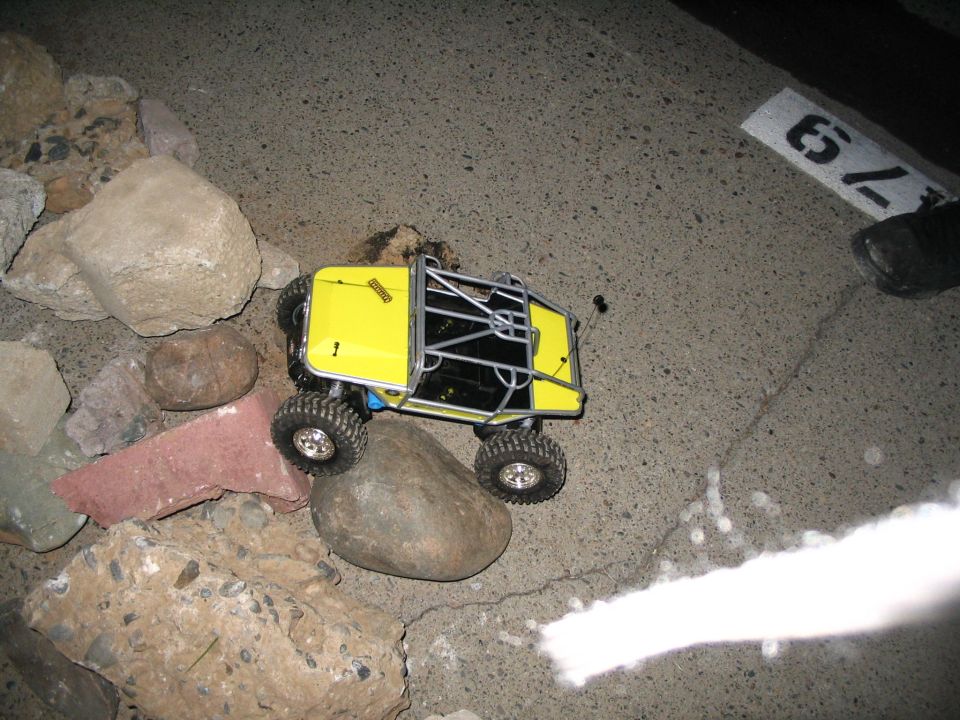 Yellow RC rock crawler with silver tube cage on rocks at night, a number sign reading 79 nearby