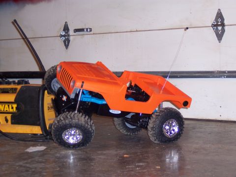 1988 Ford Bronco - An orange RC crawler Jeep body sits on a chassis next to a yellow DeWalt tool.
