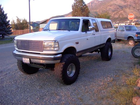1992 Ford F-150 - A white 1992 Ford F-150 pickup truck with a camper shell is parked on a gravel lot with another truck in the background.