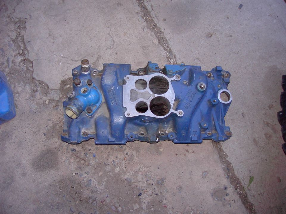 Blue intake manifold with a silver gasket and various ports, resting on a concrete surface