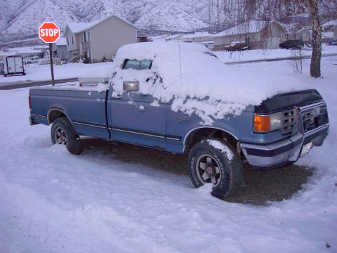 1992 Ford F-150 - A blue 1992 Ford F-150 pickup truck is parked on a snowy street, partially covered in snow.