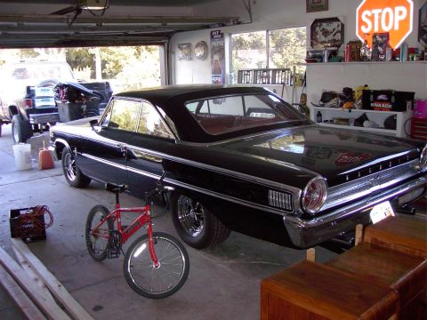 1992 Ford F-150 - A black 1964 Ford Galaxie 500 is parked in a garage next to a red bicycle and a pickup truck.