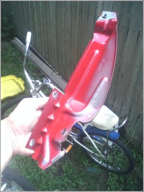2005 Chevrolet Cavalier - A red car part is held in front of a wooden fence and a bicycle.