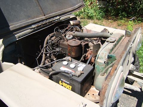 1950 Jeep CJ5 - The engine bay of a Jeep shows its 6-volt battery, radiator, and various engine parts under the hood.