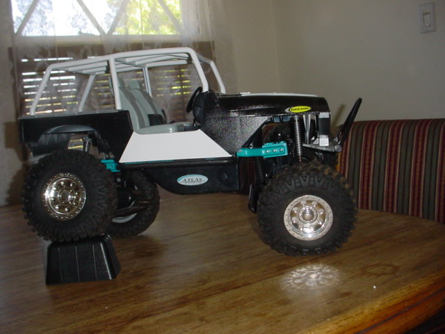 RC crawler model with white roll cage and black body, sitting on a wooden table
