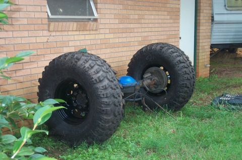 1987 Ford Bronco - This image shows a rear axle assembly with oversized tires, likely for an off-road vehicle, resting on grass next to a brick building.
