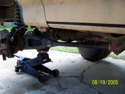 1987 Ford Bronco - A vehicle's undercarriage is shown supported by a blue hydraulic jack, highlighting suspension and drivetrain parts.