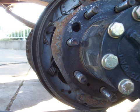 1994 Ford F-150 - Close-up of a rusty drum brake backing plate, wheel hub and lug studs on a vehicle axle being serviced.