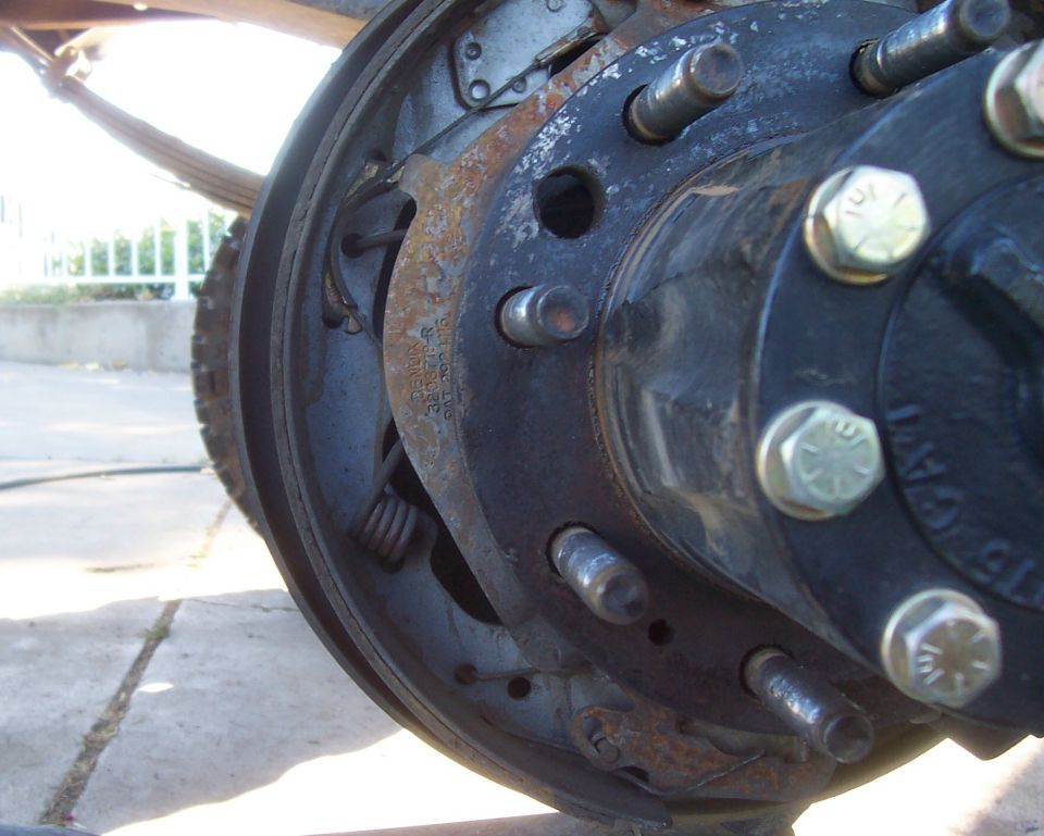 Rusty rear drum brake backing plate and lug studs on a truck axle
