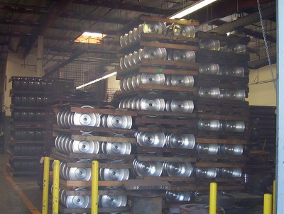 1995 Ford Bronco - Numerous aluminum wheels are stacked on wooden pallets inside a warehouse, with a SuperMotors logo visible at the bottom right.