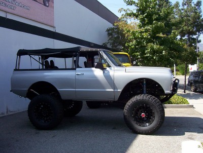 1995 Ford Bronco - A lifted Chevrolet K5 Blazer with a black soft top is parked outside a building.