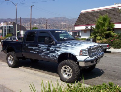 1995 Ford Bronco - A lifted pickup truck with custom graphics is parked on the side of the road in front of a building.