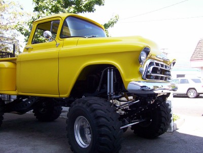 1995 Ford Bronco - A bright yellow pickup truck is heavily modified with a lift kit and oversized tires, parked outdoors.