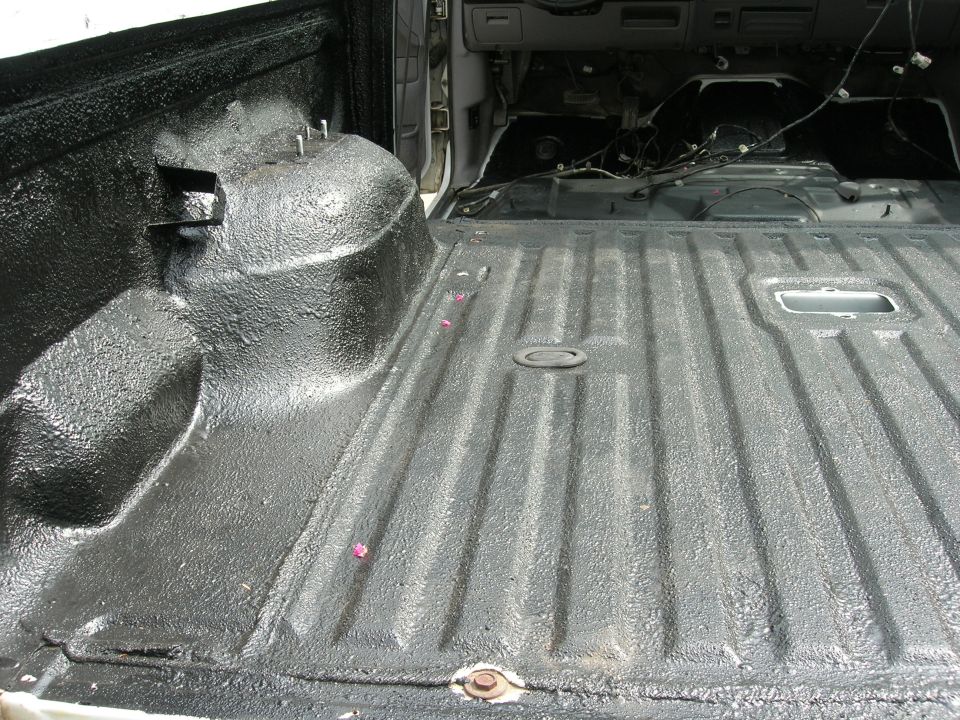 Truck bed interior with black spray-on liner, showing wheel well and interior cabin