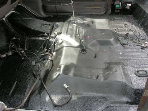 1994 Ford Bronco - The interior floor of a vehicle has been stripped down to the metal and coated with a black protective material, with wiring exposed.