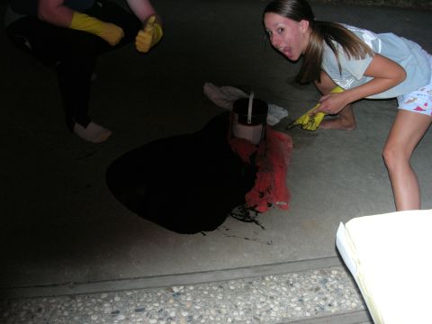 1994 Ford Bronco - People are applying a black coating to a car part, with some of the coating spilled on the ground.