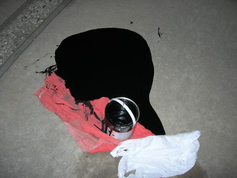 1994 Ford Bronco - A can of black paint has spilled onto a rag and the concrete floor, with a plastic bag nearby.