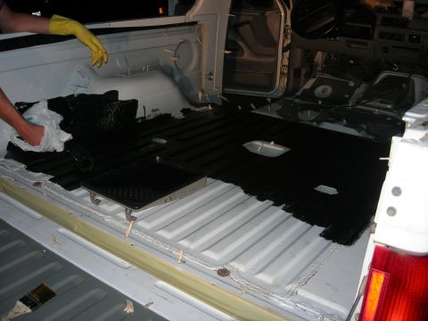 1994 Ford Bronco - A truck bed's interior is being coated with a black protective material, with a person in yellow gloves applying it.