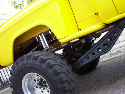 1995 Ford Bronco - Close-up view of the massive tires and suspension system of a yellow monster truck.