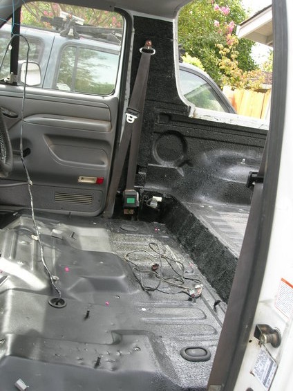 1991 Ford Bronco - Interior view of a pickup truck with seats removed, showing the floor and wiring. Another vehicle is parked nearby.