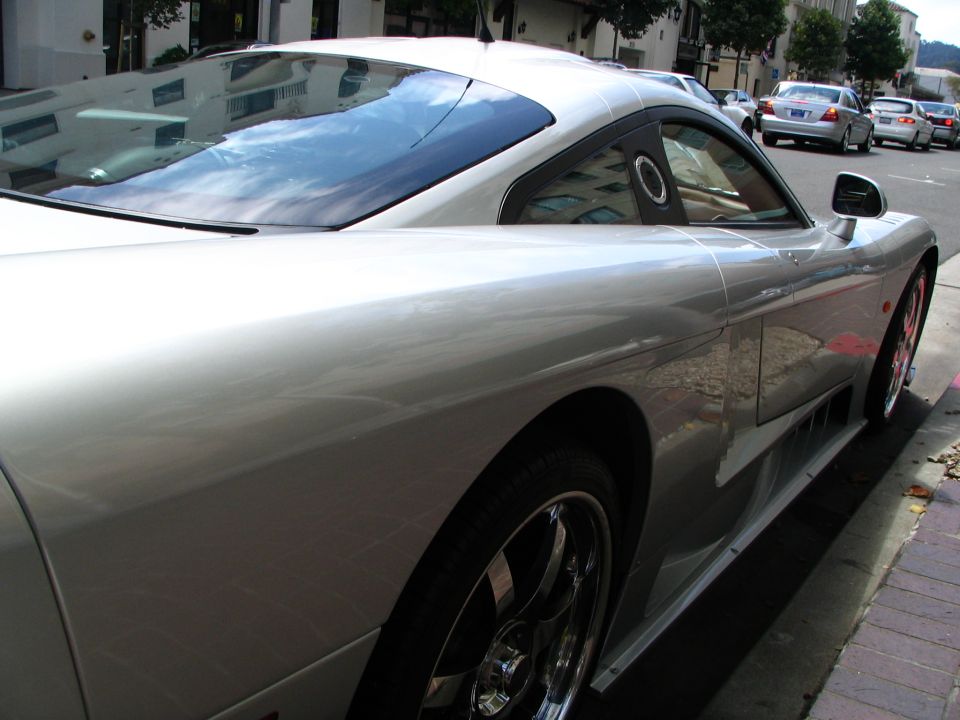 Side view of a silver sports car parked on a city street, with other cars in the background