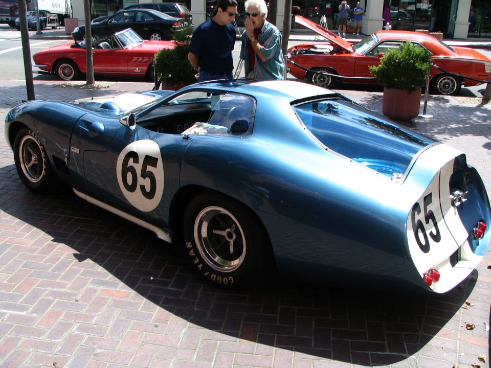 Blue race car with white stripe and number 65 on door and rear. Other cars visible in background