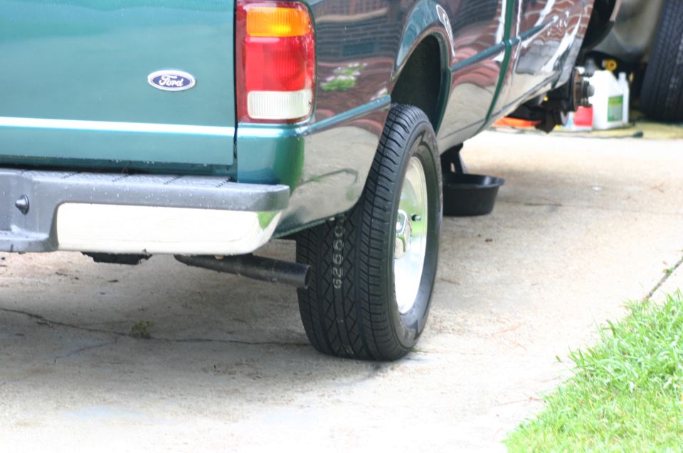 Rear driver's side of a green Ford Ranger pickup truck, showing the tailgate, bumper, and wheel. The Ford logo is visible on the tailgate