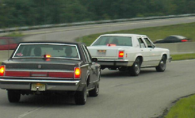 Rear view of a dark sedan and a white sedan on a track