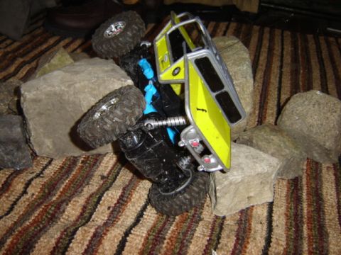 1992 Ford Bronco - A yellow toy truck is stuck on rocks, with its wheels in the air.