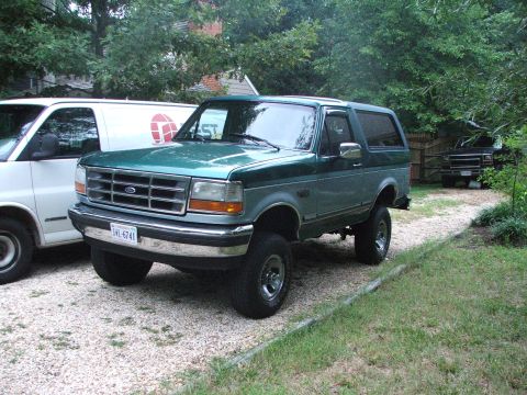 1996 Ford Bronco - This 1996 Ford Bronco is parked on a gravel driveway with a white van to its left and another vehicle in the background.