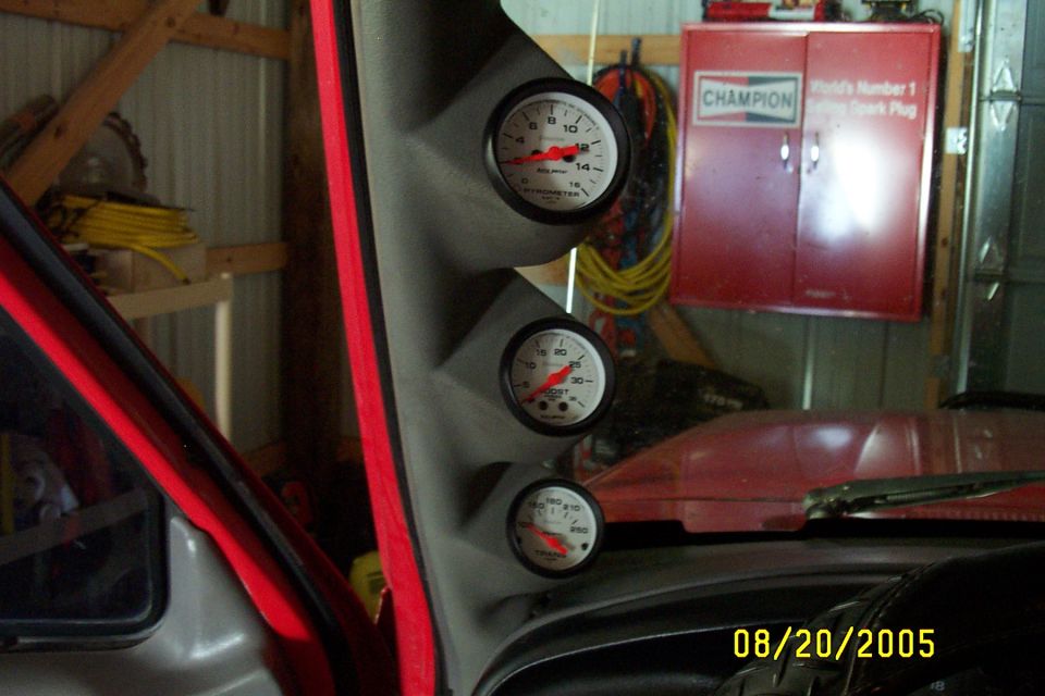 Interior view of a red vehicle with three gauges mounted on a gray pillar, dashboard visible