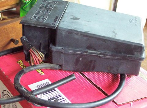 1985 Ford Crown Victoria LTD - A black fuse box with visible wiring and labels is shown, resting on a red box.