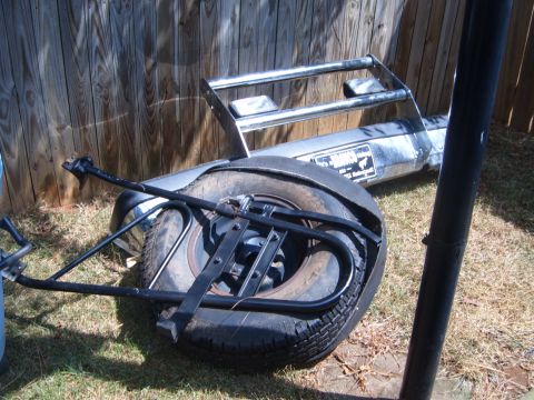 1988 Ford Bronco - Spare tire and bumper are lying on the ground next to a wooden fence.