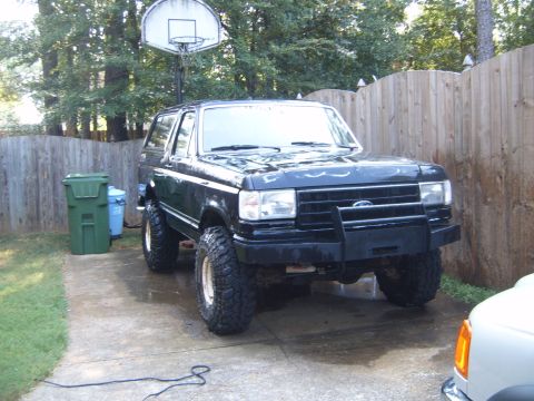 1988 Ford Bronco - This lifted black Ford Bronco is parked in a driveway with a basketball hoop and trash cans nearby.