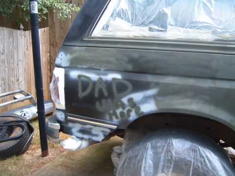 1988 Ford Bronco - The rear of a vehicle is covered in primer and has spray-painted text on the side.