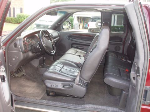 1995 Ford Bronco - The interior of a red Dodge Ram pickup truck is shown, with a view of the dashboard and seats. A white SUV is parked outside.