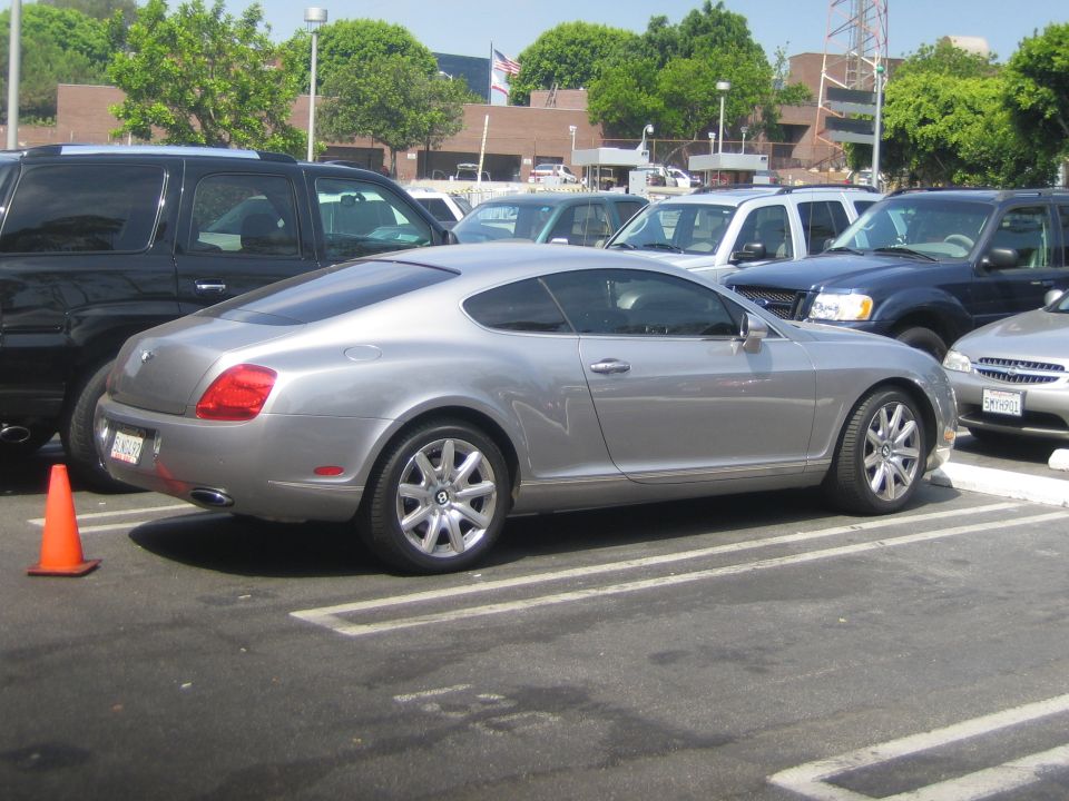 Silver Bentley Continental GT coupe parked in a lot, other vehicles visible