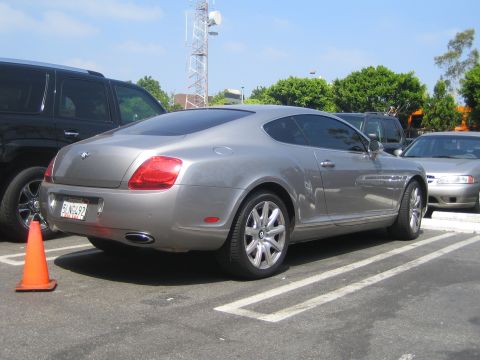 1968 Ford Mustang - A silver Bentley Continental GT is parked in a lot, with other vehicles nearby.