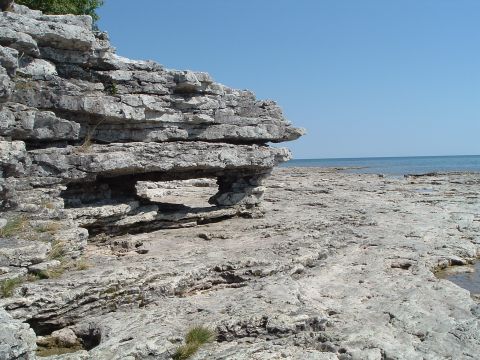 1995 Mercury Grand Marquis - A scenic view of a rocky shoreline with layered rock formations leading to the ocean under a clear blue sky.