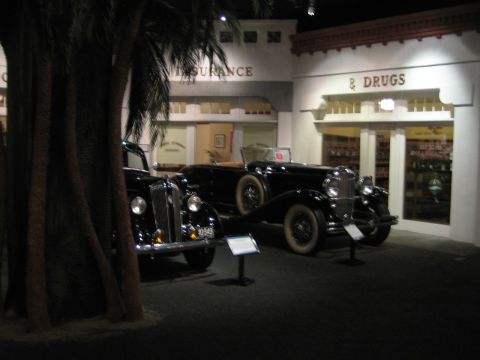 1968 Ford Mustang - A museum exhibit recreates a street scene with two classic automobiles displayed in front of vintage storefronts.