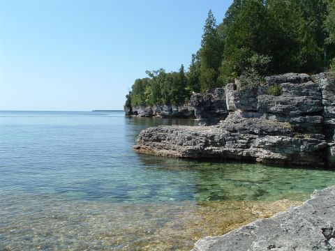 1995 Mercury Grand Marquis - A scenic view of a rocky shore meeting clear, calm waters, with lush trees on the cliffs above.